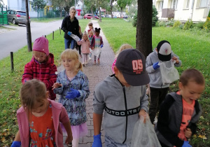 Dzieci idą chodnikiem. Każdy ma rękawiczkę jednorazową, a niektórzy niosą foliowe torebki.