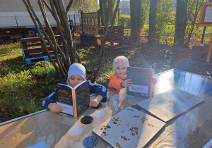 Dzieci oglądają książki przy stoliku w ogrodzie.