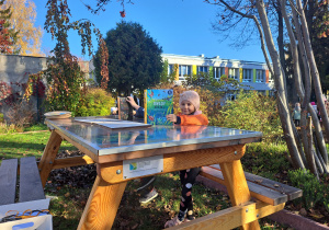 Dzieci oglądają książki o tematyce przyrodniczej siedząc przy ławostole w ogrodzie przedszkolnym.