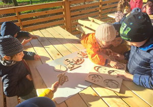 Dzieci układają drewniane puzzle warstwowe przy sole w altanie.