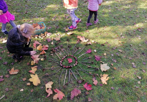 Dzieci układają mandalę z kolorowych liści, szyszek, kasztanów i patyków.