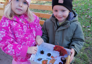 Dzieci trzymają przygotowaną jesienną kompozycję w pudełku.