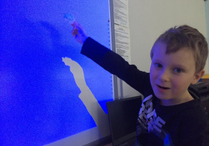 Chłopiec trzyma w dłoni zastygniętą bryłę wosku na tle tablicy interaktywnej.