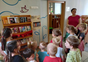 Grupa dzieci stoi przed regałem z książkami.