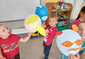 Grupa dzieci siedzi na dywanie. W rękach trzymają zwierzątka zrobione z balonów.
