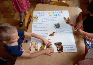 Dzieci przy stoliku przygotowują plakat informujący o akcji charytatywnej na rzecz schroniska dla zwierząt.