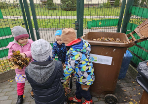 Dzieci przerzucają liście z taczki do pojemnika na odpady biodegradowalne.
