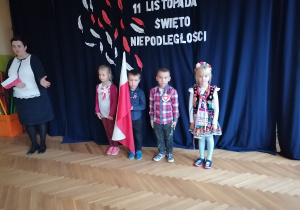 Czworo dzieci z flagą Polski na tle dekoracji. Obok nich Pani Dyrektor.