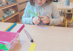 Dziewczynka koloruje mazakami kółeczka na małej kartce papieru.