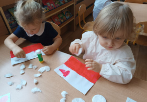 Dwie dziewczynki wyklejają białą część flagi Polski płatkami kometycznymi.