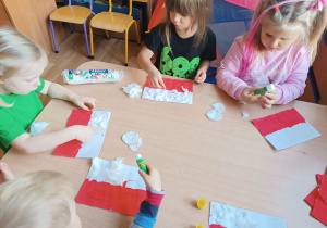 Dzieci przy stoliku wykllejają flagę Polski.