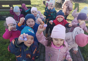 Grupa dzieci stoi na chodniku i trzyma nad głową kolorowe, styropianowe jajka.