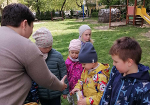 Pani dyrektor wręcza chłopcu nagrodę w ogordzie przedszkolnym. Obok nich znajduje się kilkoro innych dzieci.