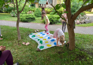Dwie dziewczynki grają na trawie w grę twister.