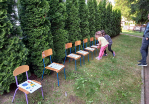 Dwie dziewczynki oglądają plansze z figurami geometrycznymi ułożone na krzesełkach.