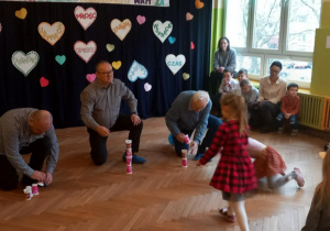 Dziadkowie ustawiają na podłodze wieżę z papierowych kubeczków podawanych przez wnuki.