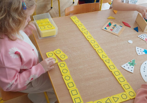 Dziewczynka przy stoliku układa domino z figurami geometrycznymi.