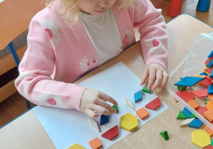 Dziewczynka układa na kartce kompozycję z drewniamych klocków.