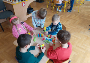 Dzieci przy stoliku układają budowle z kolorowych, drewnianych klocków.