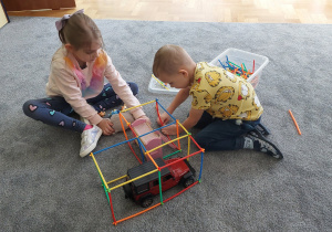 Dwoje dzieci buduje garaż dla samochodu z klocków- patyków.