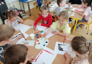 Dzieci przy stolikach malują farbami.