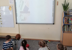 Dzieci oglądają wyświetlony na tablicy obraz przedstawiający kompozycję z kwadratów i prostokątów.