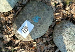 Kamień z narysowanym niebieską kredą rysunkiem prezentu i przyklejoną kartką z rysunkiem prezentu.