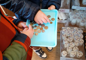 Dzieci wybierają monety z niebieskiej tacy.