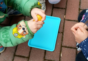 Dzieci kucają dookoła tacy. Chłopiec otwiera plastikowe jajko.
