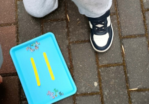 Dzieci kucają obok tacy, na której w dwóch zbiorach leżą liczmany - kaczki. Pomiędzy zbiorami znajduje się ułożony z kolorowych patyczków znak równości.