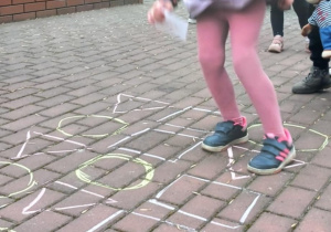 Dziecko stoi na trójkącie narysowanym kredą na kostce brukowej.