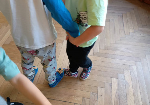 Dwoje dzieci trzyma się za ręce i dotyka stopami.