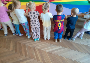 Dzieci stoją w kole i trzymają chustę animacyjną.