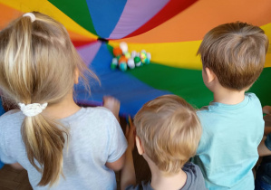 Dzieci trzymają chustę animacyjną, na której leżą piłki różnej wielkości.
