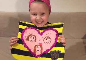 Dziewczynka prezentuje swój herb, czyli serce z trzema portretami na żółto-czarnym tle.