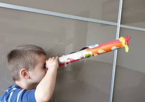 Chłopiec patrzy przez długą lunetę zrobioną z papierowych rolek.