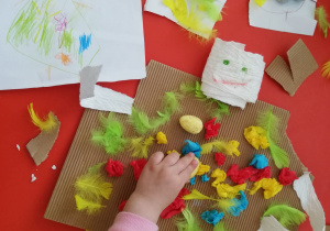 Dziecko przykleja różne materiały do kawałka tektury falistej.