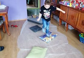 Chłopiec chodzi po poduszkach, pod którymi rozłożony jest biały materiał.
