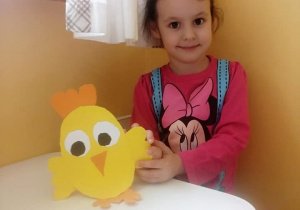 Dziewczynka prezentuje wyciętego z papieru żółtego kurczaka.