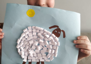 Chłopiec prezentuje pracę plastyczną - baranka z pasków papieru.
