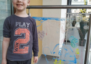 Chłopiec namalował farbami obrazek na szklanej osłonie na balkonie.
