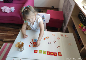 Dziewczynka układa kartoniki z liczbą elementów.